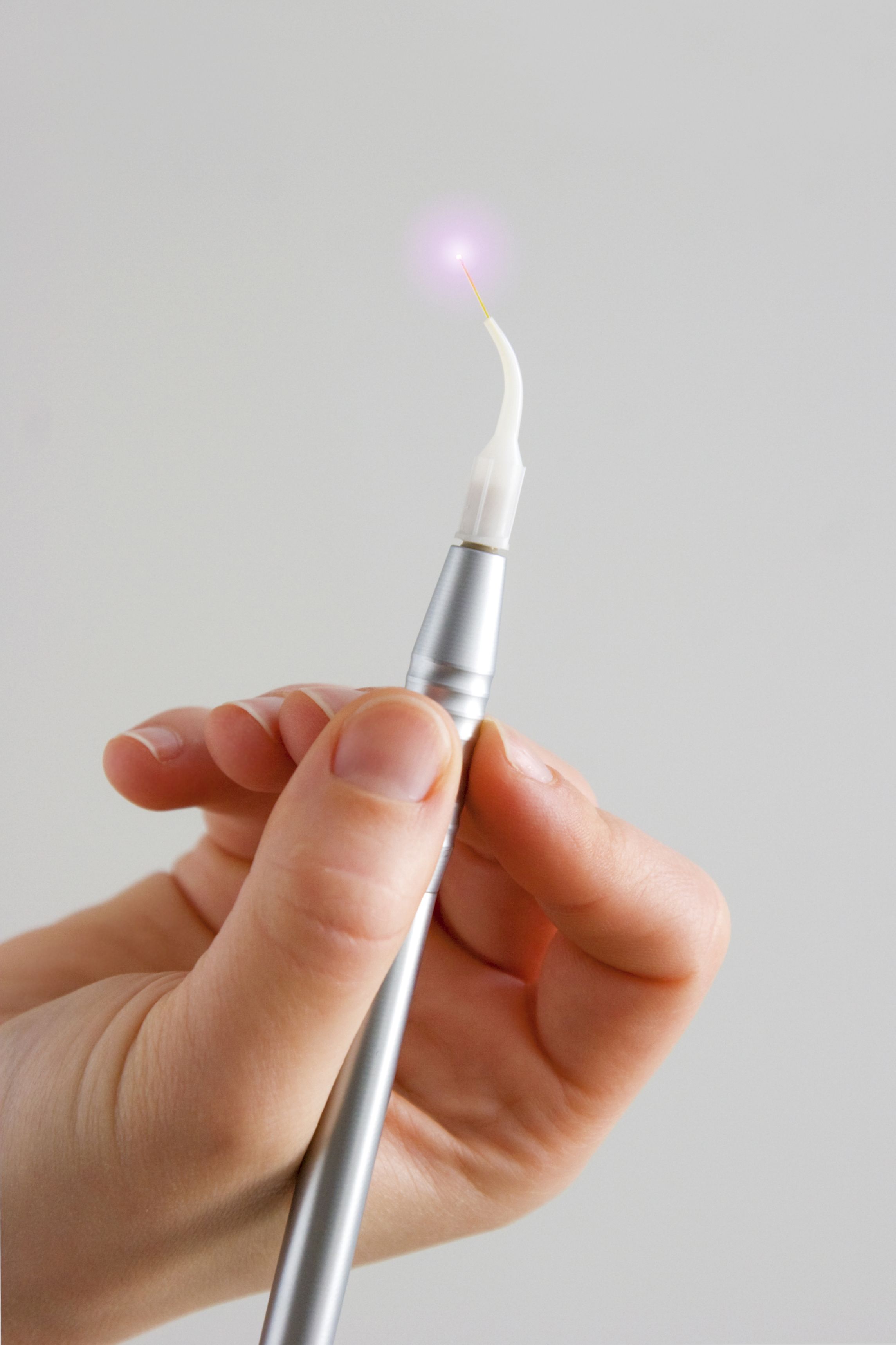 A close-up of a person’s hand holding an illuminated dental laser. 