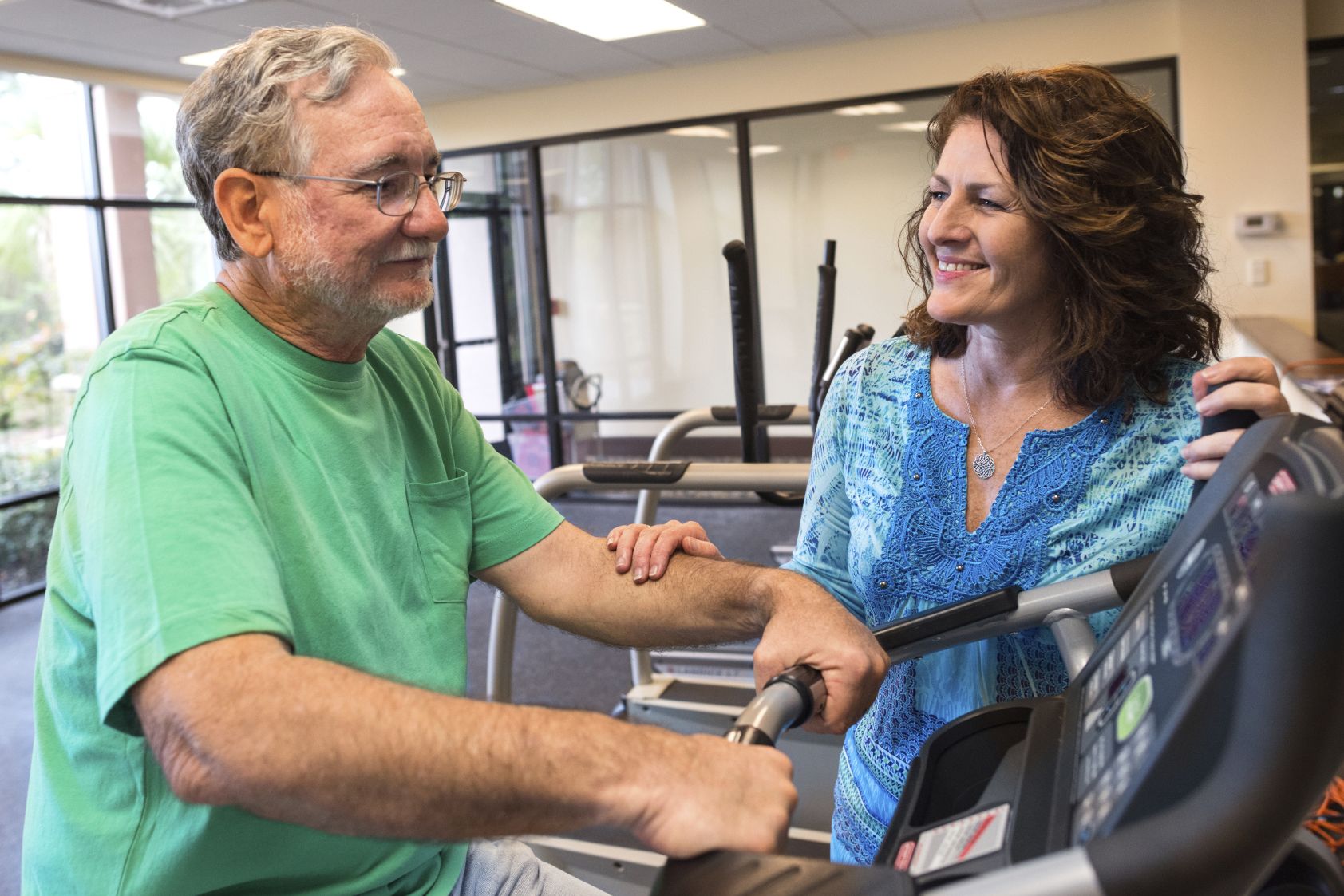Grey-haired man on a treadmill who is supported by a woman