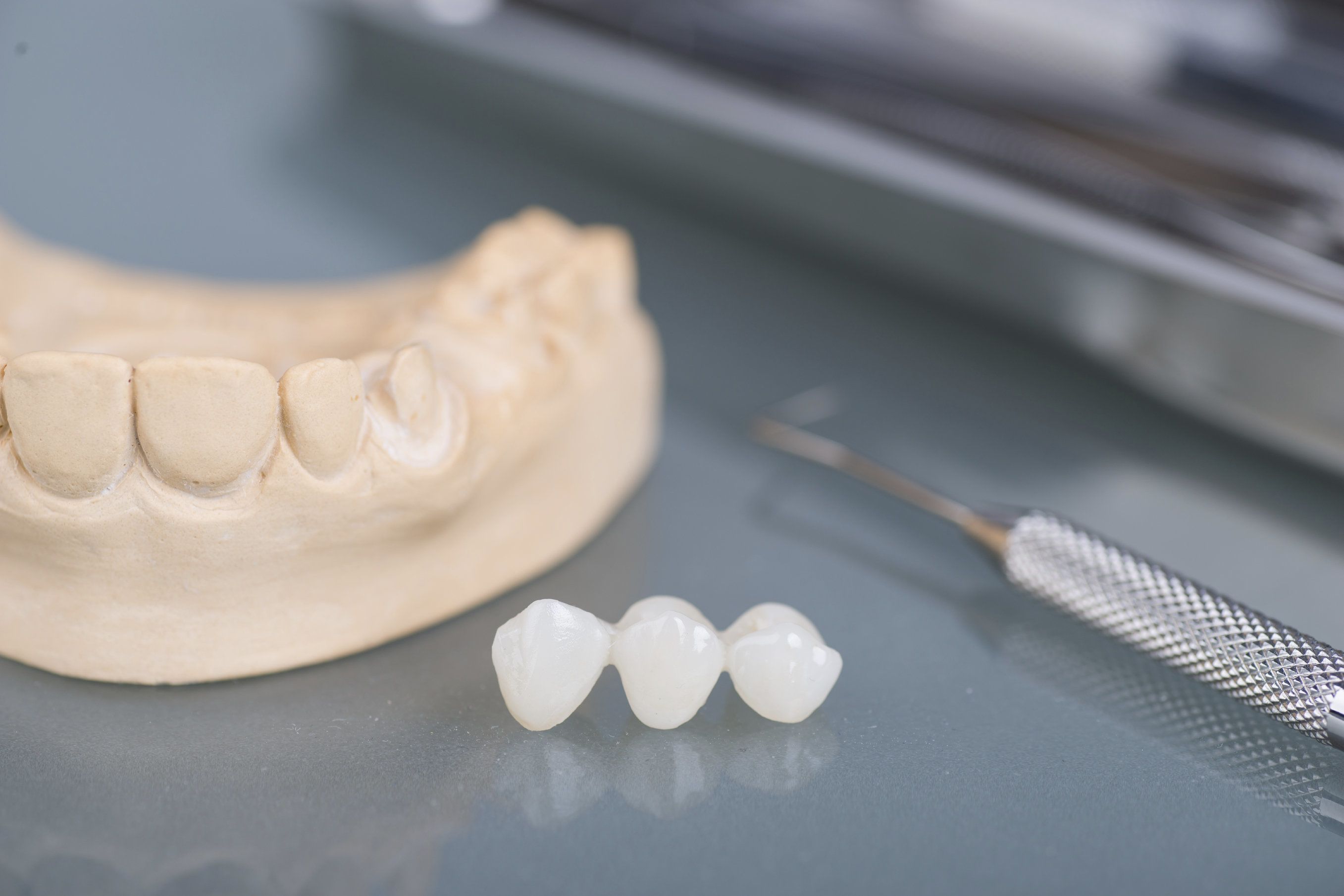 model of jawbone, dental bridge, and lab instrument laying on reflective gray surface