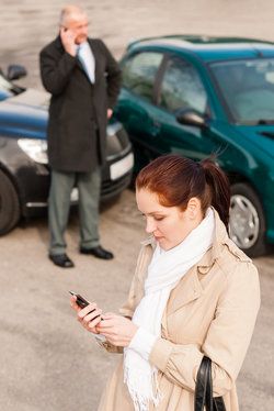 A woman using her phone at the scene of a car accident