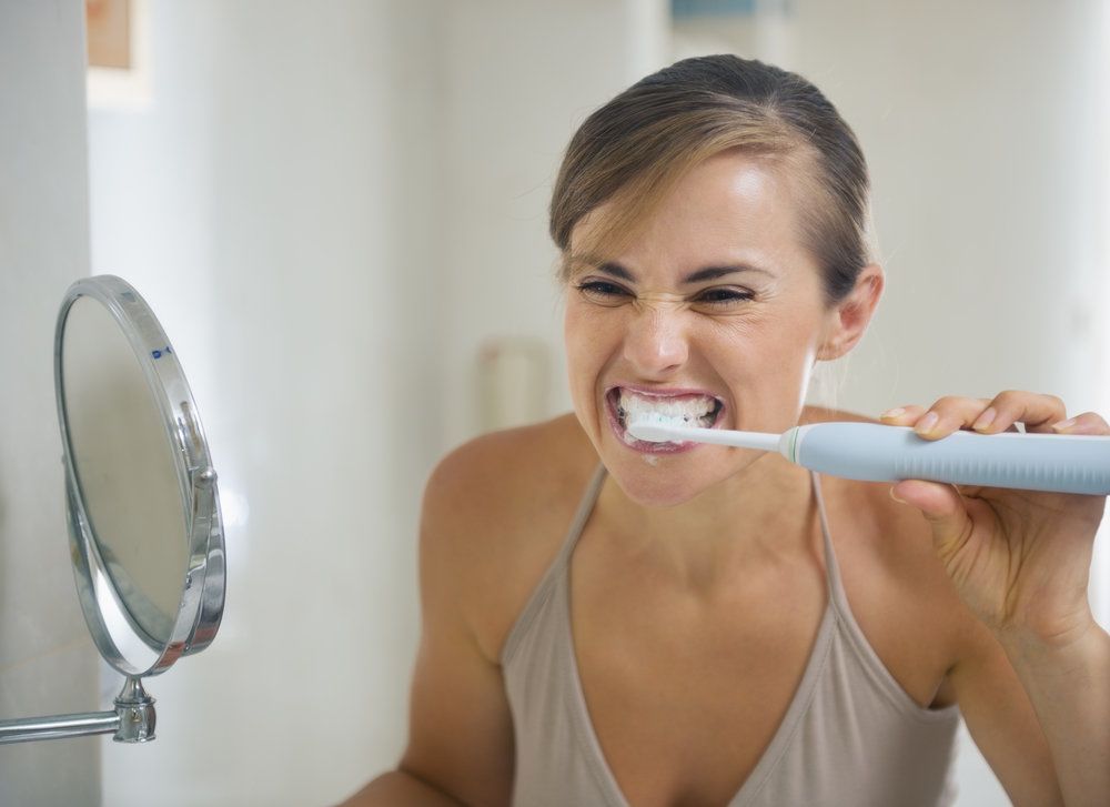 Woman brushing her teeth with electric toothbrush in front of bathroom mirror