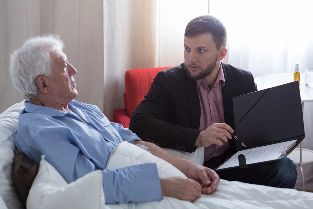 elderly man in bed writing a will with an attorney