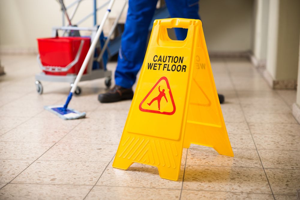 person mopping and “caution wet floor” sign