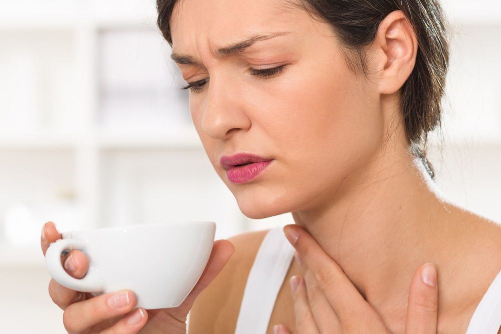 Woman holding a teacup with one hand to her throat