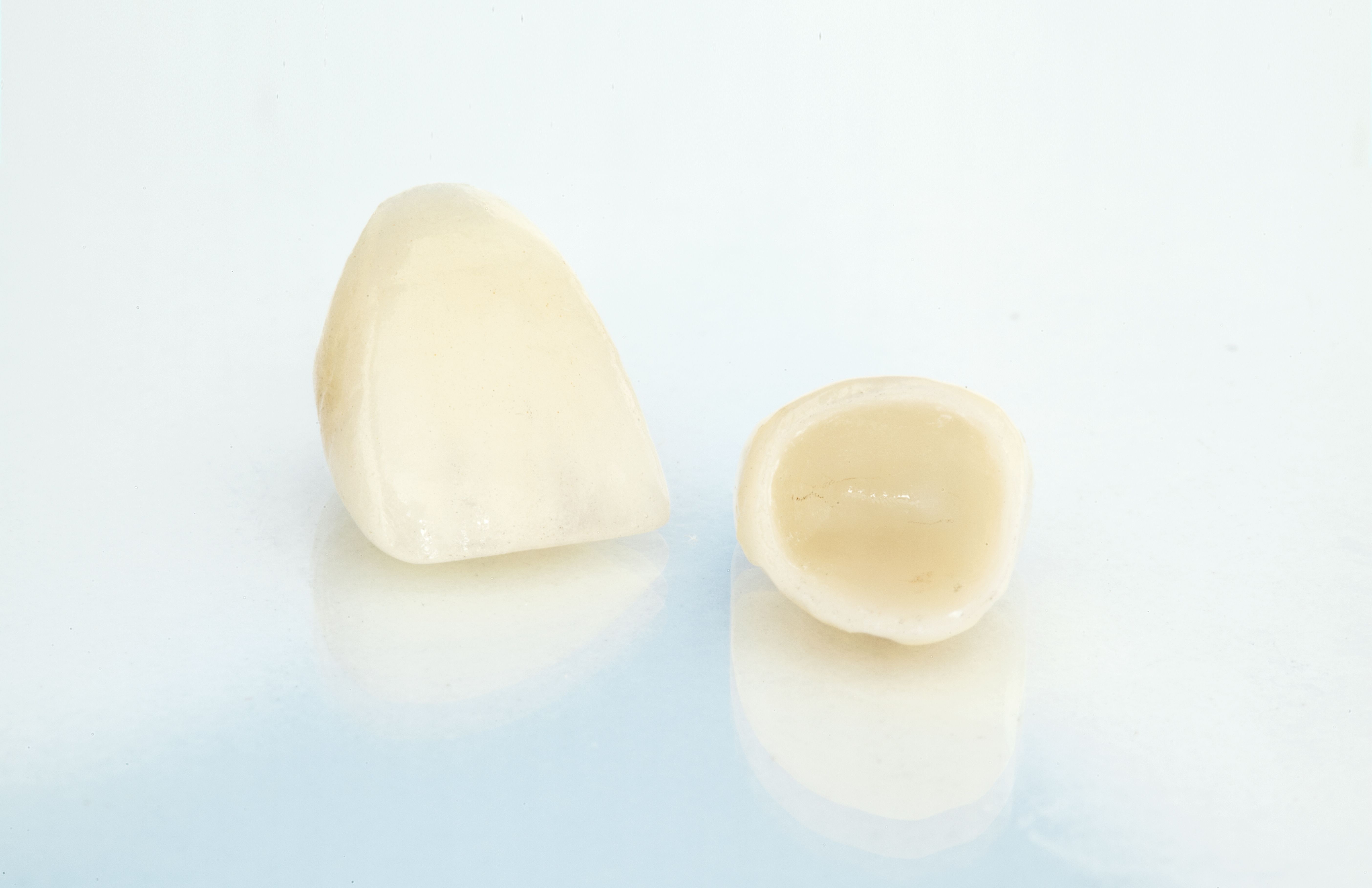 Two dental crowns on plain reflective white surface