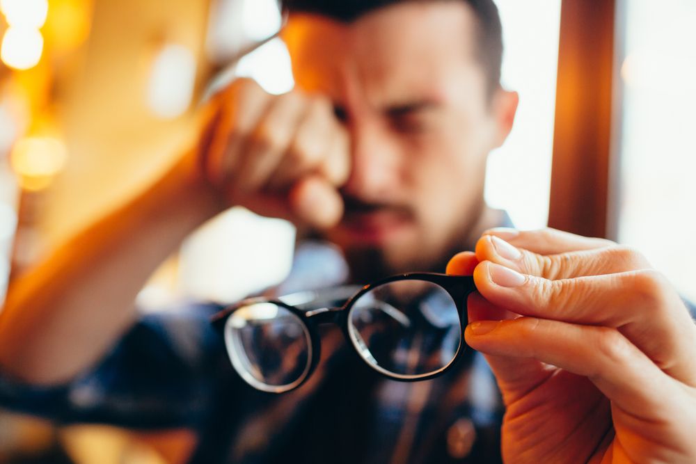 A man holding glasses and rubbing his eyes