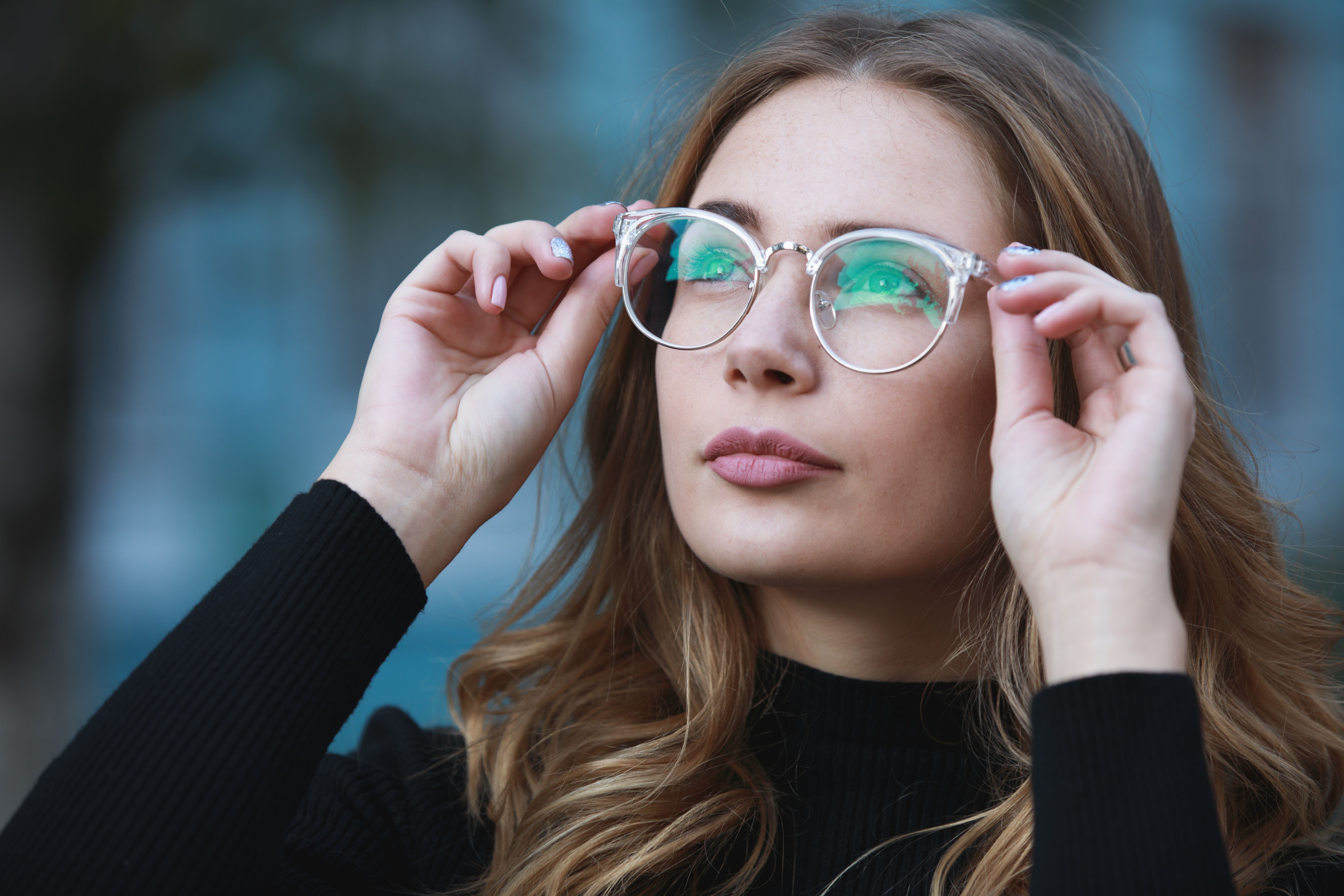 woman looking up while putting on eyeglasses
