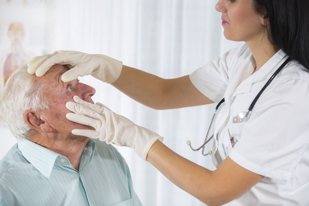 medical professional holding open older male patient’s eye