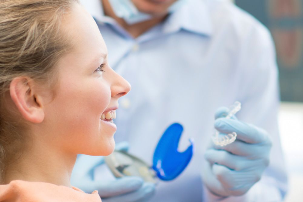 A young female smiles as a dentist hands her a new Invisalign clear aligner