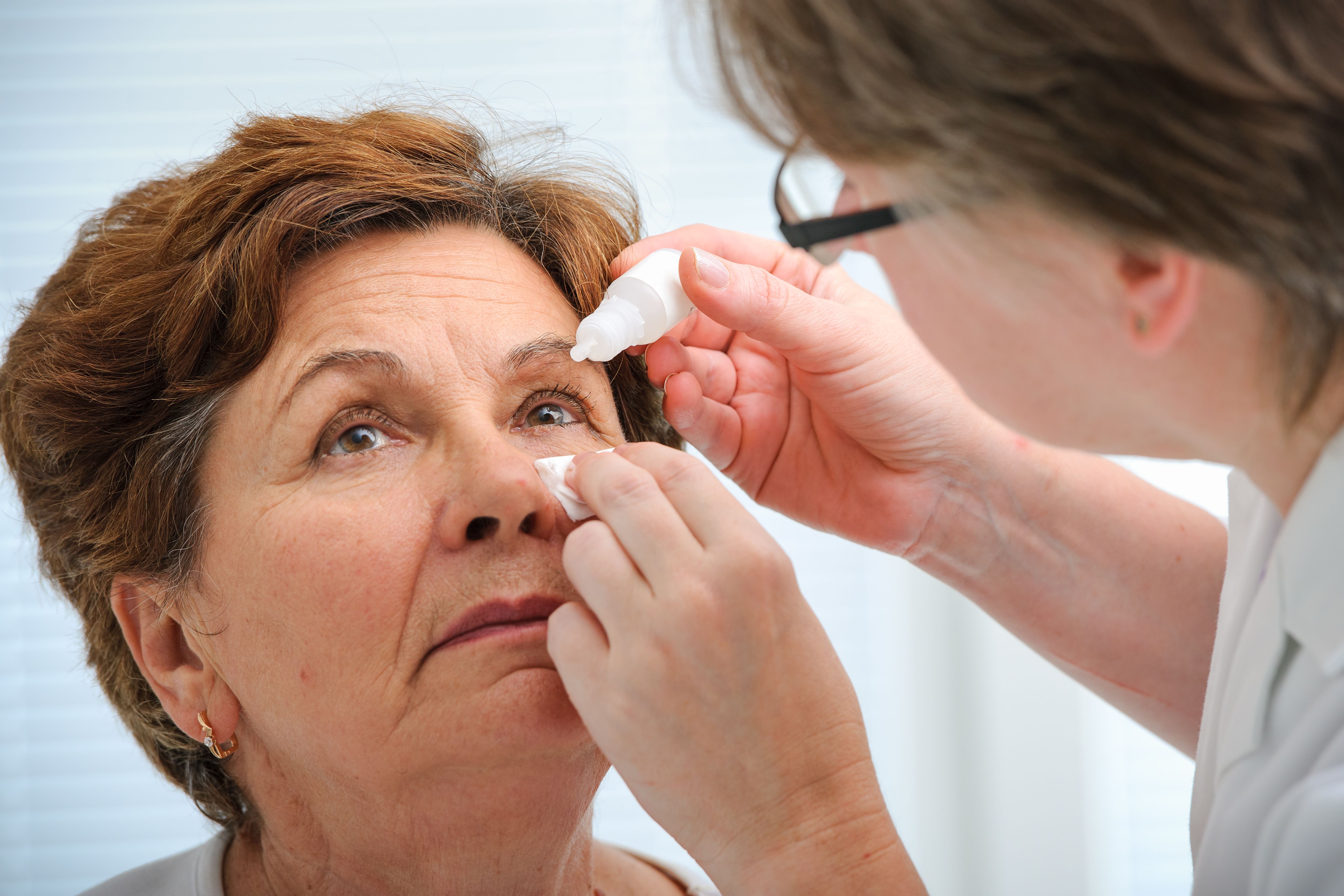 Closeup of a woman getting eye drops put into her eye by a doctor